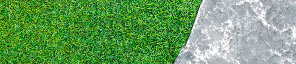 Surface texture of concrete walkway flooring beside the plastic artificial grass of lawn